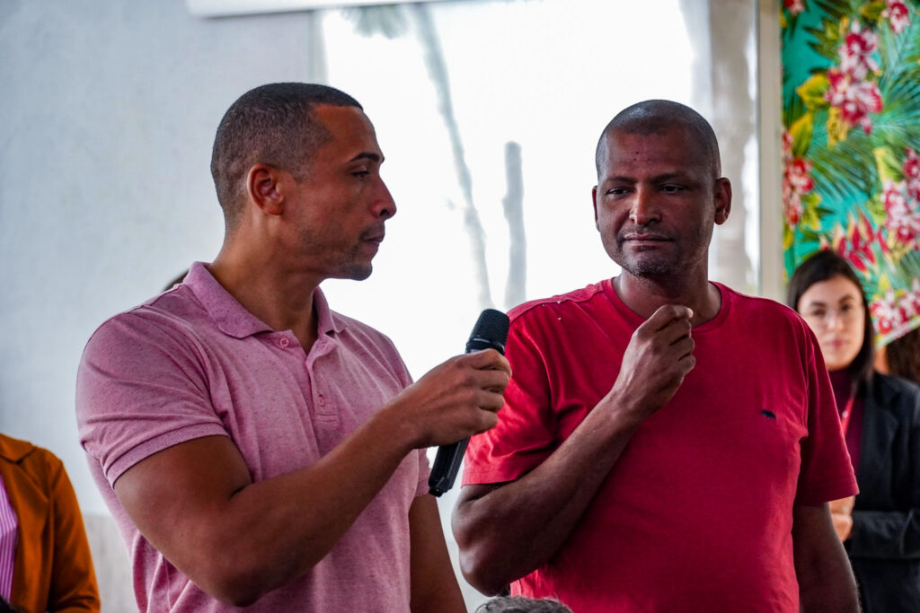 Os atingidos Cássio e Ernane, de Ipaba, falam durante a reunião. Cássio segura o microfone e está prestes a entregá-lo para Ernane.