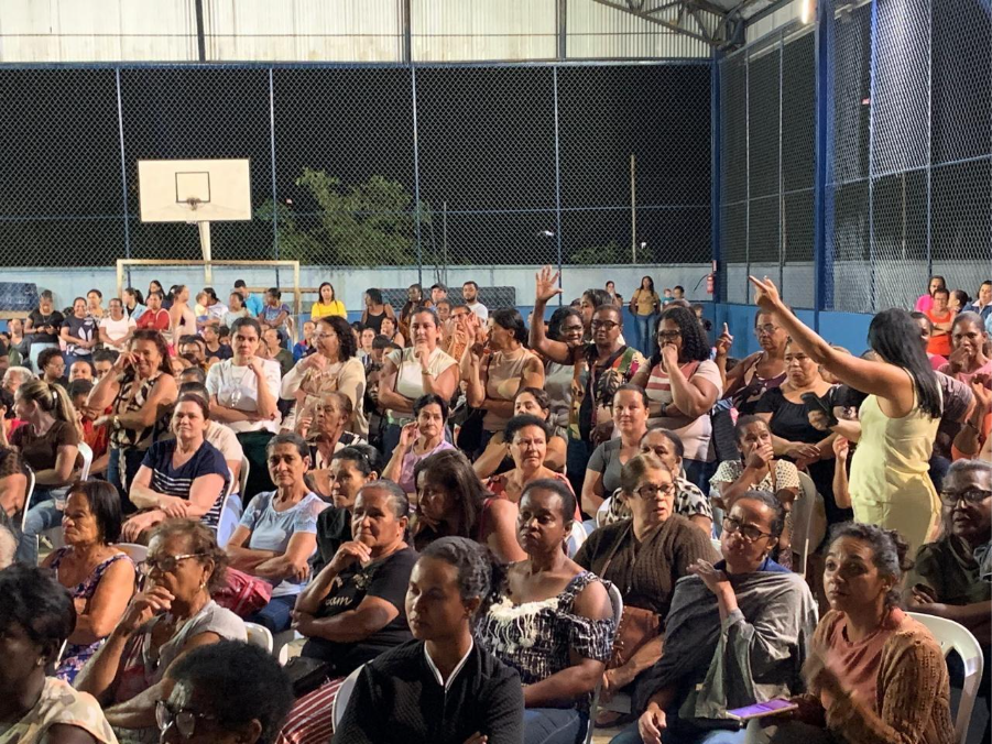 Atingidas de Barra Longa estão em reunião num ginásio. Algumas estão com as mãos levantadas, enquanto uma delas diz algo.
